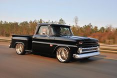 an old black pickup truck driving down the road