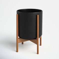 a black planter with wooden legs on a white background in the shape of a pot