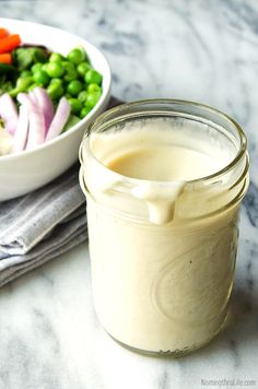 a glass jar filled with dressing next to a bowl of vegetables