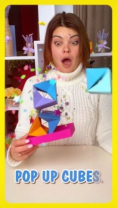 a woman holding up some colorful objects in front of her face with the caption pop up cubes