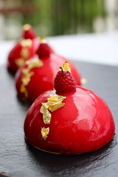 three chocolate covered desserts with raspberries and gold leaf decorations on them sitting on a table