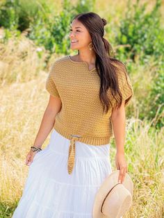 a woman in a dress and hat walking through tall grass