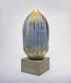 a blue and gold vase sitting on top of a wooden block in front of a white background