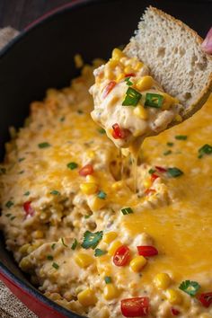 a hand holding a tortilla chip over a skillet filled with corn and cheese