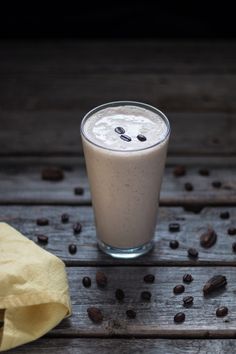 a glass filled with liquid sitting on top of a wooden table next to coffee beans