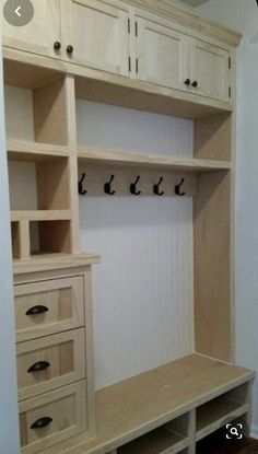 a wooden shelf with drawers and hooks on the wall next to a white cabinet in a room