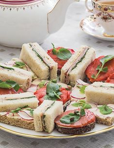 a plate with sandwiches and tomatoes on it next to a teapot filled with watermelon