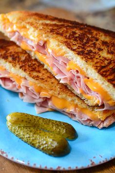 a grilled ham and cheese sandwich on a blue plate with pickles