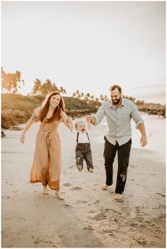 a man and woman holding hands as they walk along the beach with their toddler