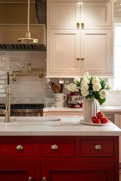 a kitchen with white and red cabinets and flowers in a vase on the counter top