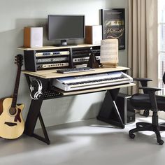 a computer desk with a keyboard, monitor and guitar