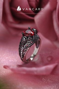 a red diamond ring sitting on top of a pink rose petals with the words vancaro written below it