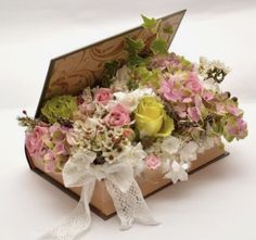 an open box filled with lots of flowers on top of a white table next to a ribbon