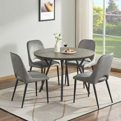 a dining room table with four chairs and a rug in front of the window,