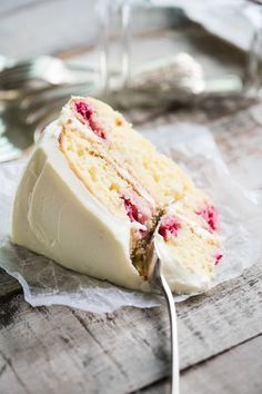 a piece of cake with white frosting and raspberries on it is being held by a fork