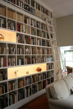 a living room filled with lots of white bookshelves next to a wall full of books