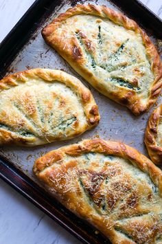 four baked pastries sitting on top of a baking pan covered in cheese and spinach