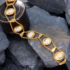 This elegant bracelet features seven oval shell cameos bezel-set along chain and teardrop shaped gold tablets to create an undulating effect. The bracelet has French hallmarks on the slide-in clasp. The bracelet is crafted in 18k yellow gold and fits up to a 7 inch wrist. Elegant Gold Bracelet With Oval Cabochon, Elegant Yellow Gold Bracelets With Intaglio, Elegant Yellow Gold Bracelet With Intaglio, Elegant Gold Oval Cabochon Bracelet, Elegant Yellow Gold Intaglio Bracelets, Elegant Yellow Gold Intaglio Bracelet, Elegant Gold Cameo Bracelets, Elegant Gold Bracelet With Cabochon, Elegant Gold Bracelets With Cabochon