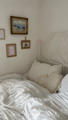 an unmade bed with white sheets and pictures on the wall