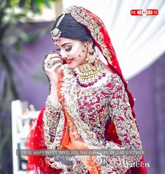 a woman in a red and gold bridal outfit talking on a cell phone while wearing jewelry