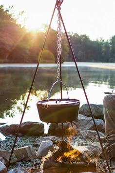 a man sitting in front of a campfire with a pot on it's stand