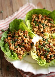 lettuce leaves with meat and seasoning on top sitting on a white plate