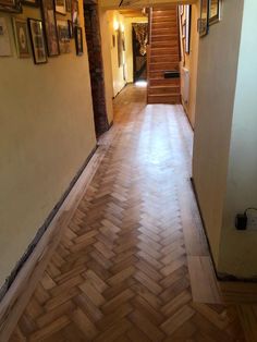 an empty hallway with wood flooring and pictures on the wall above it's stairs