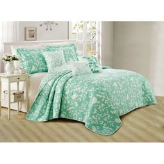 a bed covered in a green and white bedspread next to a nightstand with flowers on it