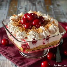 a dessert with cherries and whipped cream in a glass dish on a red napkin