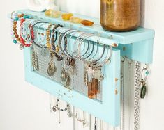 a blue shelf with lots of bracelets hanging from it's sides and a cup on top