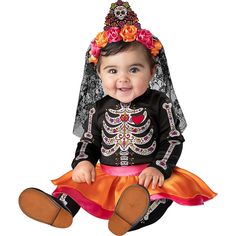 a baby dressed up as a skeleton sitting on top of a wooden floor wearing a dress and headpiece