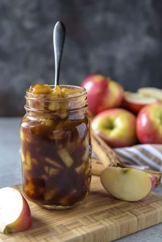 an apple jam in a glass jar on a cutting board next to apples