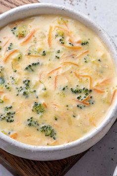 a white bowl filled with broccoli and cheese on top of a wooden cutting board