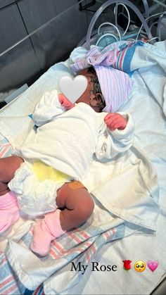 a baby laying on top of a hospital bed with a heart shaped object in it's mouth