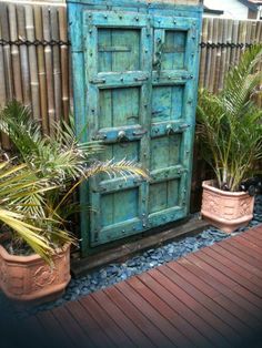 an old blue door is sitting in the middle of some plants and potted plants