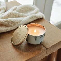 a candle sitting on top of a wooden table next to a white knitted blanket