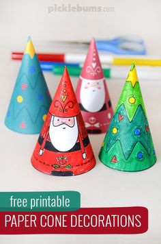 three paper cone decorations with santa clause and trees on them, sitting in front of colored pencils