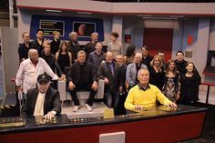 a group of people posing for a photo in front of a tv set with the crew on it