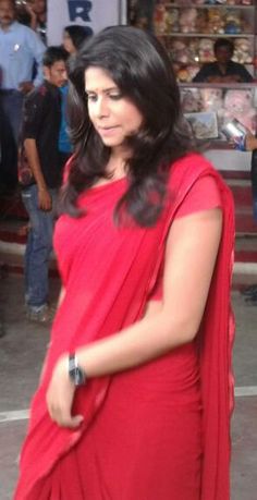 a woman in a red sari walking down the street with her hand on her hip