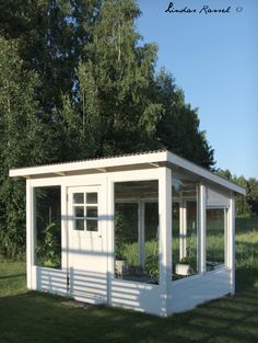 a small white building sitting on top of a lush green field with trees in the background