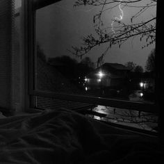 a black and white photo of a bedroom window with lightning in the sky behind it