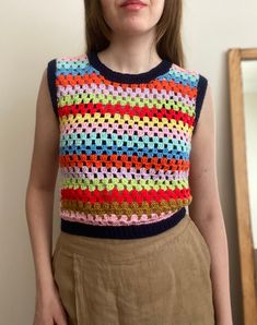 a woman standing in front of a mirror wearing a multicolored knitted top