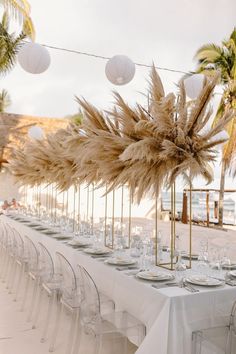 a long table is set up with white linens and tall grass centerpieces