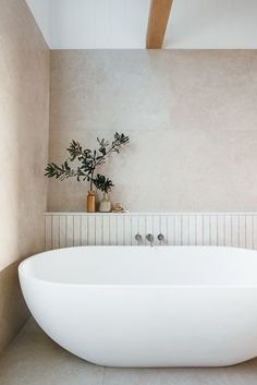 a large white bath tub sitting next to a plant on top of a tiled floor