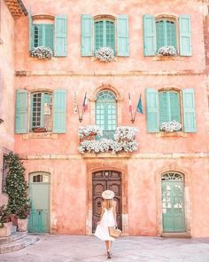 a woman walking in front of a pink building with green shutters