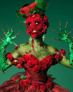 a woman dressed in green and red with hands painted like flowers on her face, holding two fingers up to the side