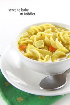 a white bowl filled with noodles and carrots on top of a green napkin next to a spoon