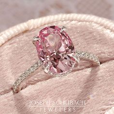 a pink diamond ring sitting on top of a cushion