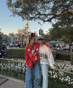 a man and woman standing next to each other in front of a castle at disneyland