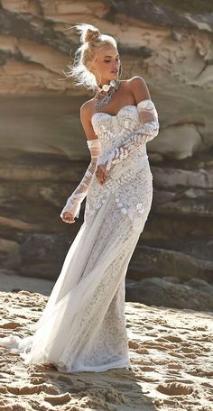 a woman standing on top of a sandy beach wearing a white dress and holding her hand out